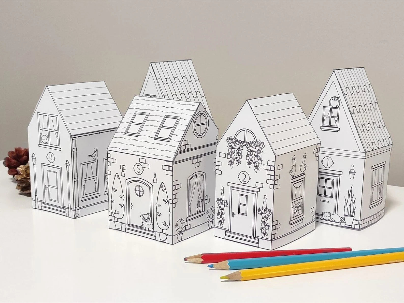 Four paper houses with coloring pages and two pencils on a white surface.