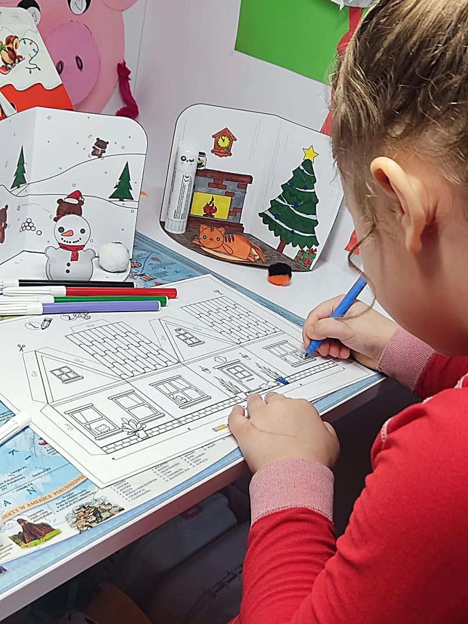 Child coloring a Christmas-themed picture with markers on a table.