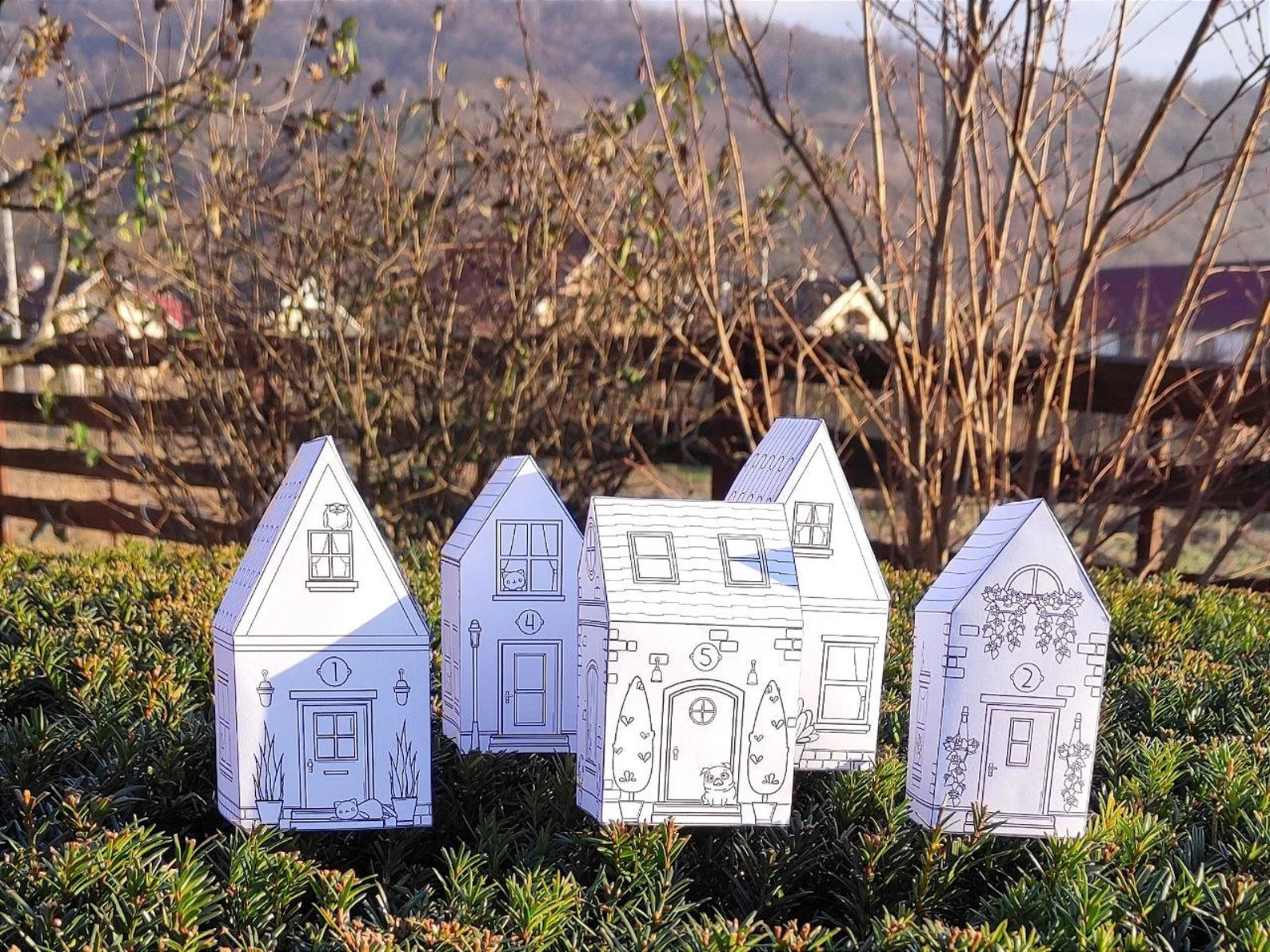 Four paper house models in a garden setting with a scenic background