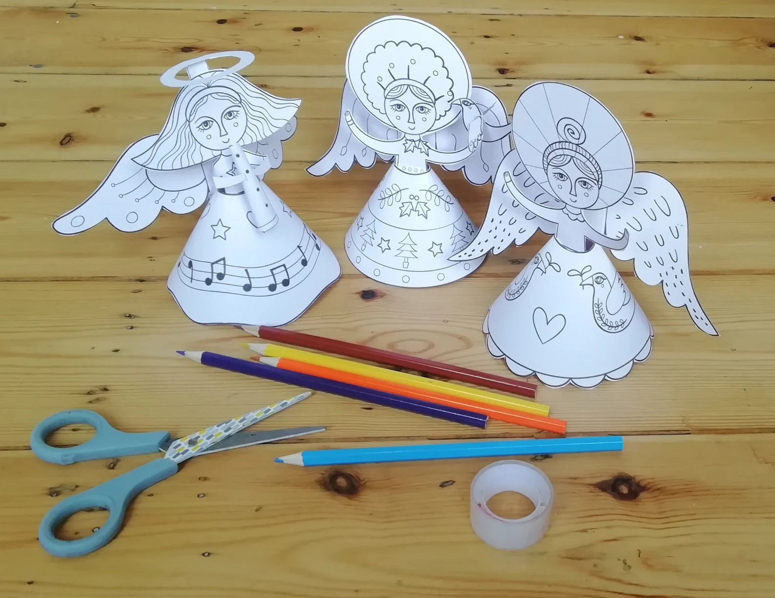 Coloring book pages of angels with coloring supplies on a wooden surface